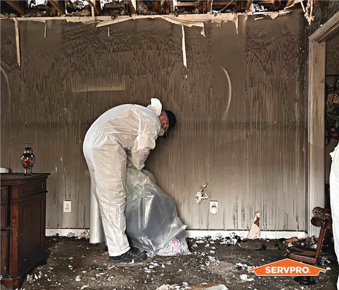 production technician bending over in a hazmat suit cleaning a fire, the walls and ceiling and floor are covered in soot