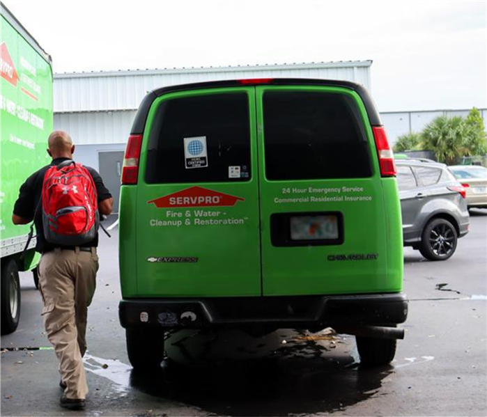 SERVPRO technician walking from a SERVPRO orange and green van to a commercial building