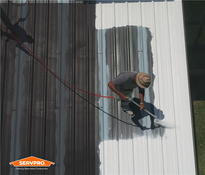 aerial shot of man coating a roof with white silicone roofing material, halfway done, Orange SERVPRO logo in corner